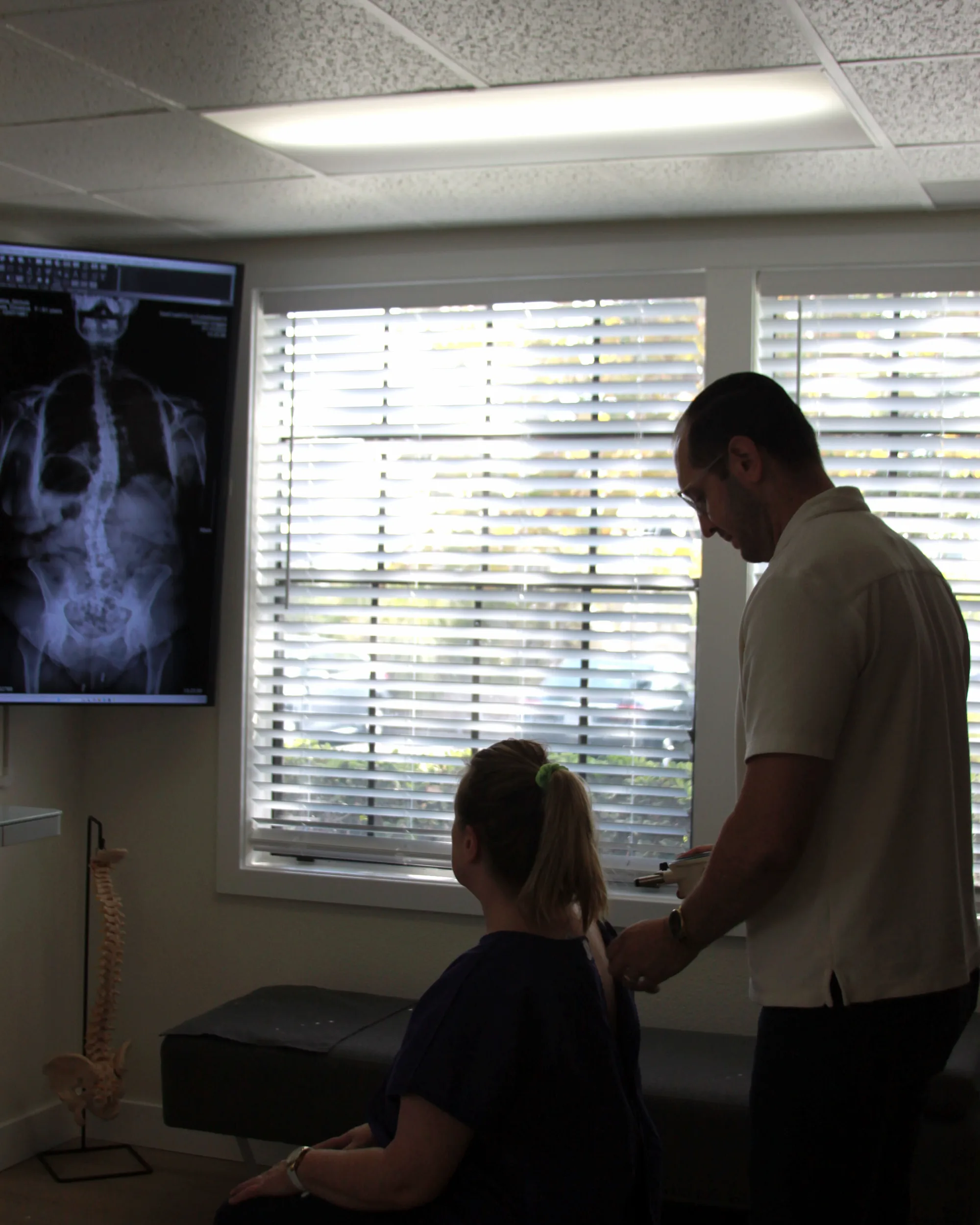 Dr. Ryan Nichols reviewing a patient’s spinal X-ray on screen with them during a consultation